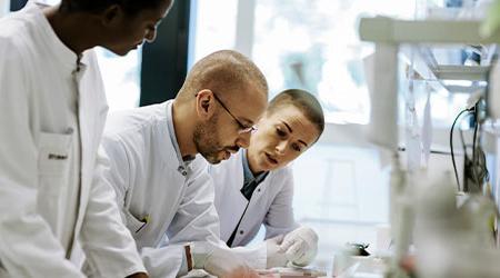 Scientists gathering around a desk station in a lab 